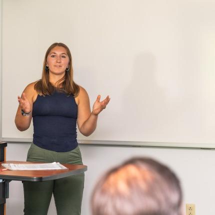 A UNE student speaks to a crowd in a classroom