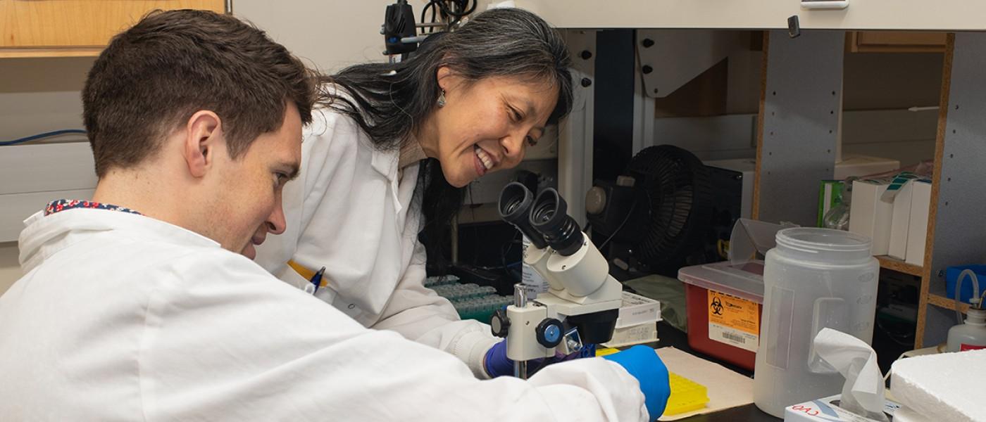 A professor helps a student prep a microscope slide